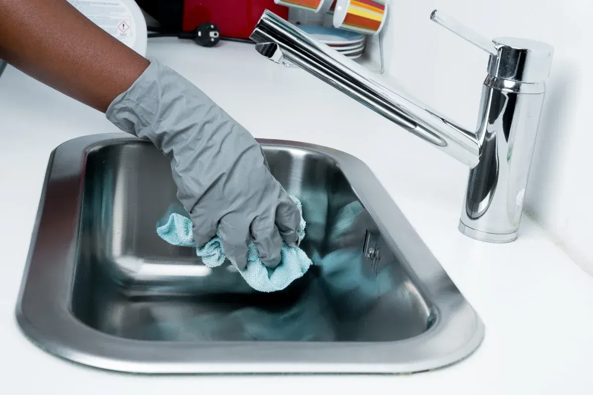 Gloved hand polishing a stainless steel kitchen sink