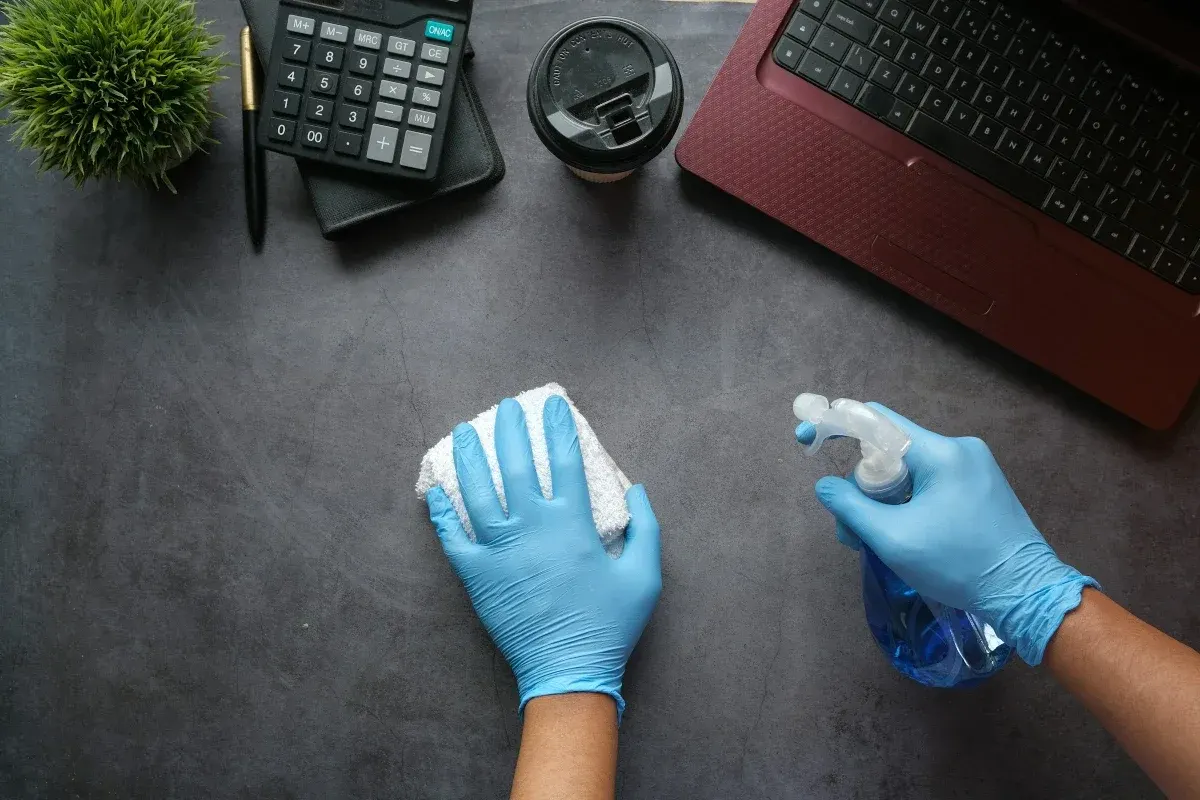Gloved hands wiping down an office desk